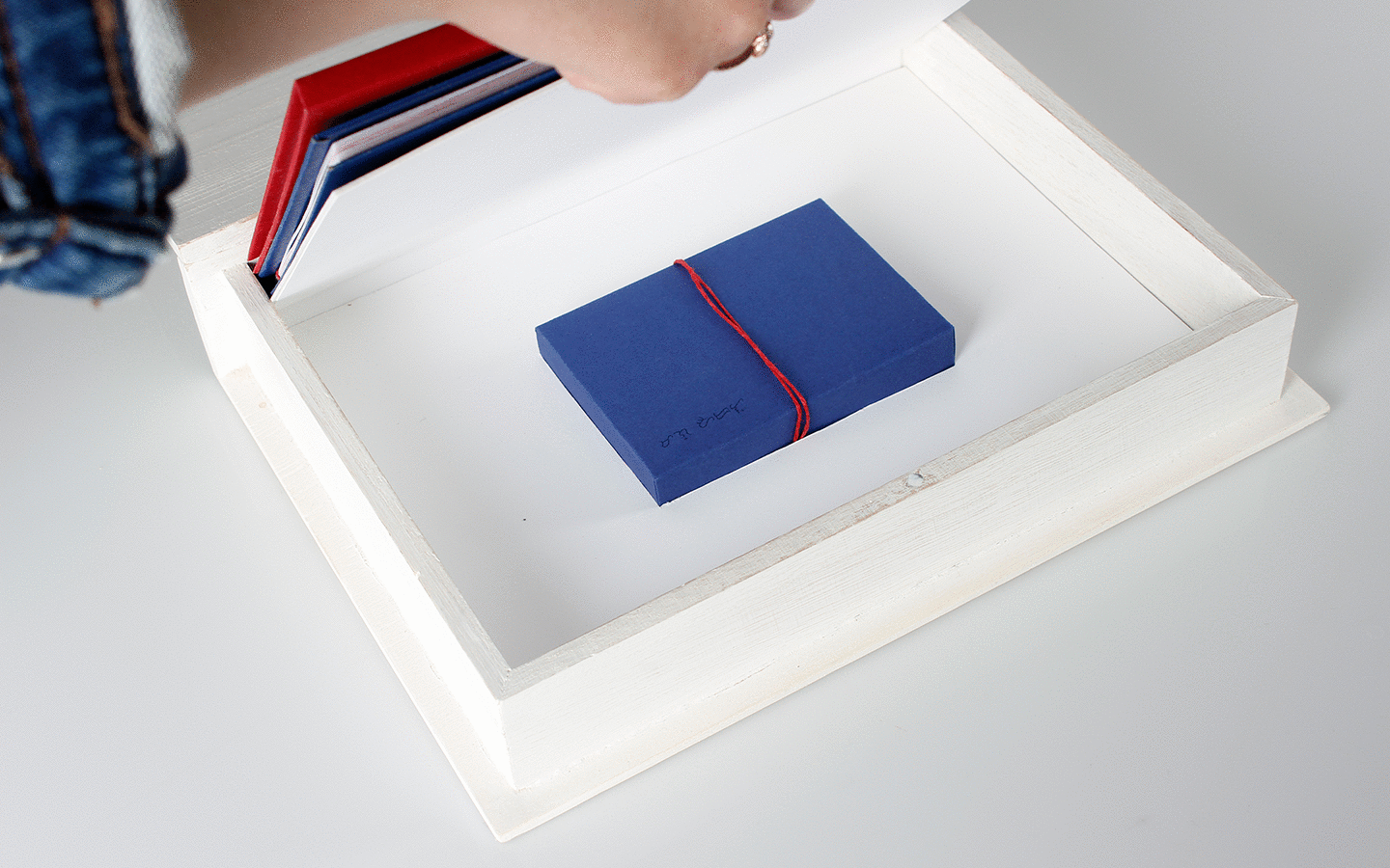 image of a hand opening a white box in order to revealing a blue box